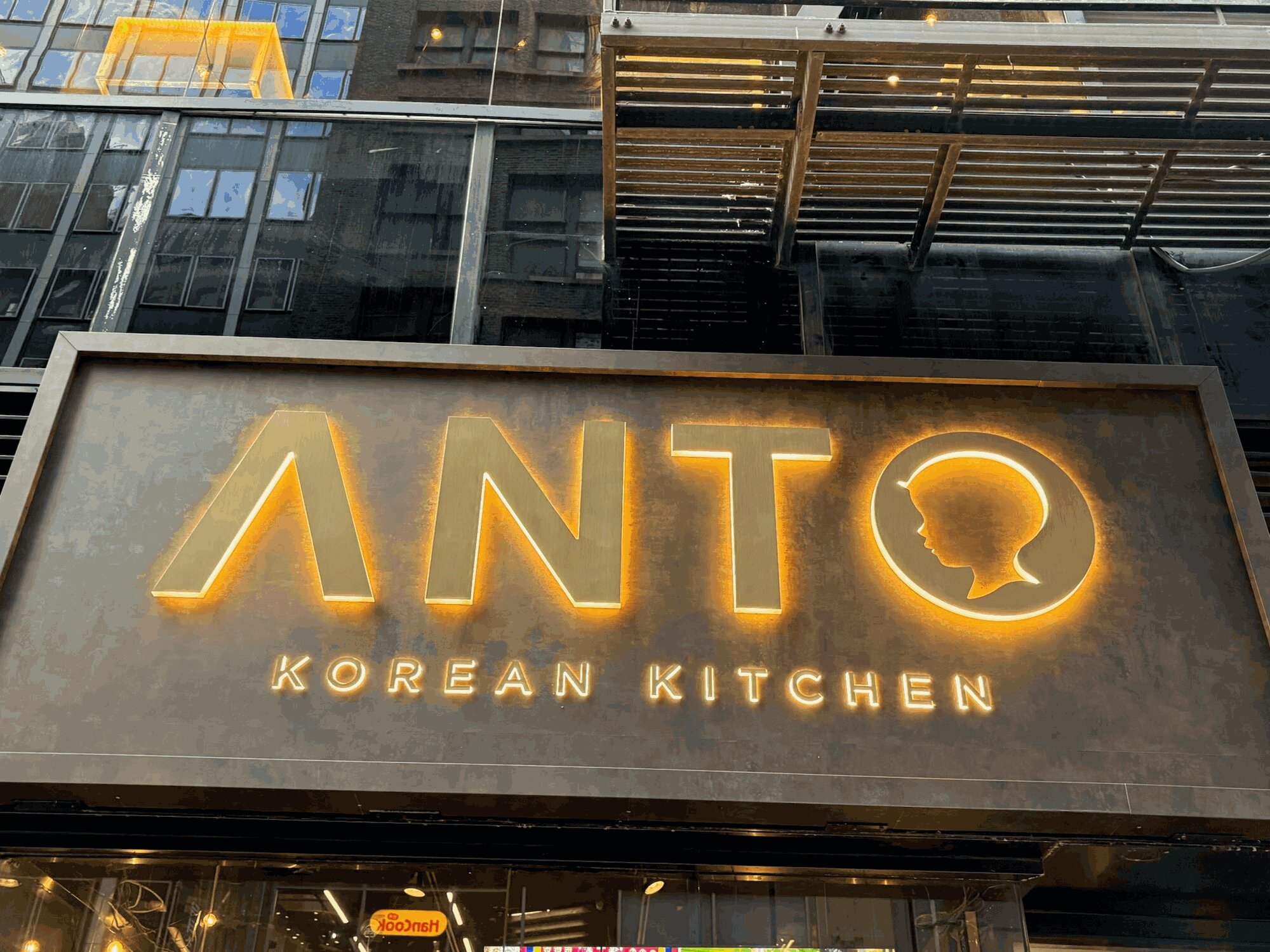 The Anto sign at 37 W 32nd Street, backlit gold letters and the child silhouette glowing on dark bronze